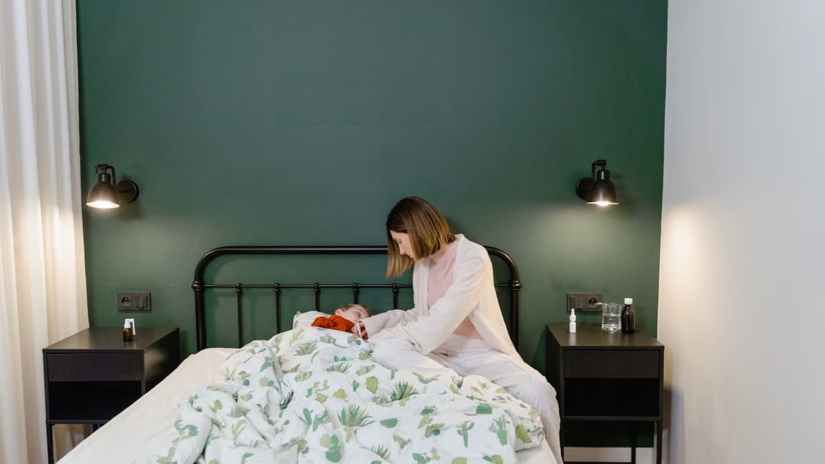 A mother cares for her child with a fever in a warm, cozy bedroom setting.